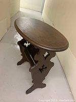 Oval dark wooden side table with integrated magazine holder and decorative carved side panels. Mark visible on the top surface.