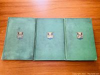 Three green hardcover books laid flat, showing front covers with coat of arms illustration.