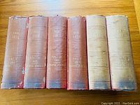 Spines of six red cloth hardcover volumes displaying gilt titles and ibis illustration