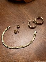 Overview of gold bracelet, hoop earrings and stud earrings on wooden surface