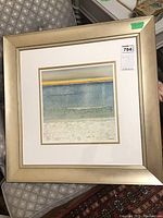 Full view of framed artwork showing beige metallic frame and white matting with gold trim.