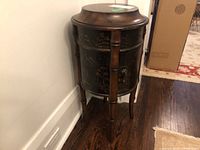 Photo of a round wooden cabinet against a wall with drawer and storage door visible