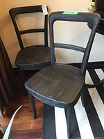Two black wooden chairs with slightly distressed finish, showing front and angled front views.