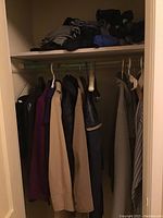 Hanging men's jackets, sweaters, and shirts in neutral and dark colors on hangers in a closet
