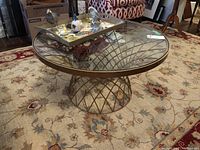 Overall front view of round coffee table showing metal lattice base and glass top with decorative tray on top.
