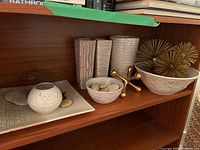 Shelf with assortment of ceramic vases, bowls, decorative stones, and gold metal accents.