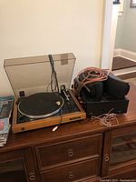 Overview of wood-plinth turntable beside receiver with cables on wooden dresser
