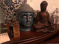 Full view of the lot showing seated Buddha figure, Buddha head bust, and three stamp-like items on a wooden surface with blue and white porcelain in background.
