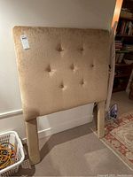 Front view of single beige tufted velveteen twin headboard with legs shown, buttons visible on surface.