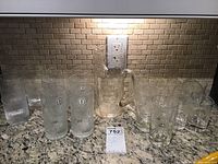 Overview of all glassware on countertop showing tall ribbed glasses, textured glasses, pitcher and etched tumblers