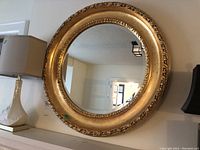 Front view of the circular mirror hung on wall above mantel with gold resin frame and beveled glass.