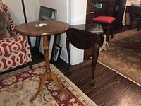 Two wooden side tables displayed near a patterned armchair and on a wood floor with area rugs, showing shape and relative size.