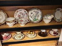 Wide shot of two wooden shelves displaying multiple porcelain teacup and saucer sets
