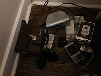 All items in the lot visible on floor corner showing Kodak Brownie camera, Canon camera with charger, two binoculars, Realistic radio, and Sony alarm clock radio.