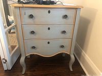 Front view of the two-tone wooden chest showing the three drawers and curved legs.