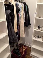 View of assorted ladies clothing items including dresses and tops hung on a rod with a box of mostly wooden hangers underneath.