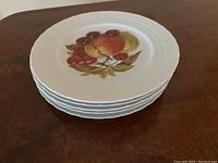 Stack of five white porcelain dessert plates with embossed rims and fruit designs in the center.