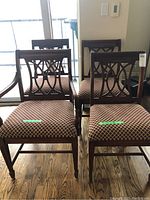 Front view of four matching wooden dining chairs with upholstered seats arranged together; dark wood finish and patterned upholstery visible.