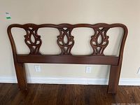 Front view of the carved wood headboard showing symmetrical carved panels and smooth dark wood finish.