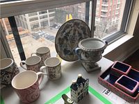 Photo showing a group of mugs, decorative pieces, and serving pieces on a windowsill with city view