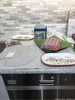Overview of lot items on kitchen counter including platters, napkins, trivet, and tin