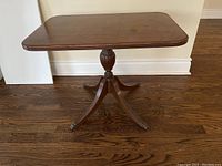 Side view showing the turned pedestal and four splayed legs with brass casters on hardwood floor.