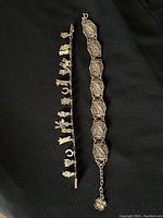 Photo showing two silver bracelets side by side on a black background, one with charms and one filigree design.
