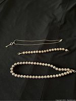 Overview of three pieces laid flat: a beaded bracelet, beaded necklace and fine chain necklace with key pendant, shown on black fabric.
