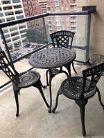 View of entire patio set from balcony, showing 26-inch round table and three chairs on concrete balcony surface