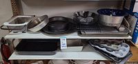 Shelf of assorted bakeware items including round pans, muffin trays, rectangular pans, cooling racks, and KitchenAid sieve.