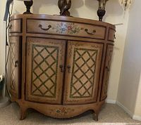 Front view of oval wooden bar cabinet with painted folk-art style design on drawers and doors.
