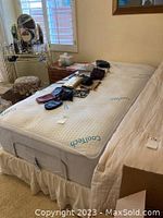 Side angle view of twin bed frame with mattress and bedding in bedroom showing adjustable head elevation and items on bed.