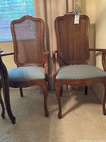 Pair of wooden captain chairs with cane backs and light blue upholstered seats, shown from an angled front view.
