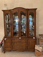 Front view of wood china cabinet showing glass display doors with shelves filled with glassware, drawers and side cabinet doors below.