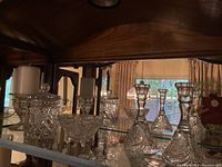 Wide view of crystal and glass items on glass shelf illuminated by natural light, showing candle stick holders, lidded containers, and decorative dish.