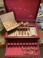 Wooden case with red felt lining holding Rogers Bros silver plated forks, spoons, and napkin holders