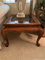 Front angle view of wooden end table showing glass inset on top and curved cabriole legs.