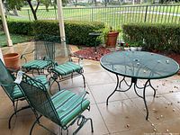 Full view of patio set showing round mesh table, four metal armchairs with mesh seats and backs, and green striped seat cushions.