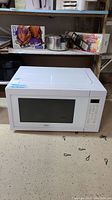 Front view of white Whirlpool microwave oven on floor with visible control panel and door