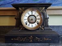 Front view of black antique mantle clock with gold decorative patterns and Roman numeral dial
