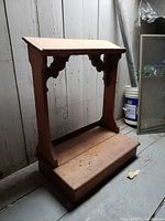 Front view of wooden church kneeler showing rectangular kneeling step and angled mantle top supported by side panels with carved Gothic braces.