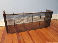 Full view of antique metal fire screen showing curved mesh design and finial accents along the top edge
