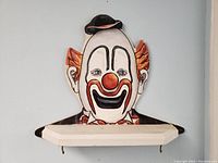 Front view of vintage Bozo the Clown face painted wood wall shelf, white shelf with hooks visible beneath