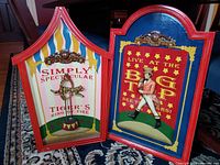 Side view of two circus advertising wall hangings side by side on floor showcasing frames and artwork