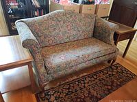 Full view of the floral patterned loveseat couch showcasing its shape and wooden legs.