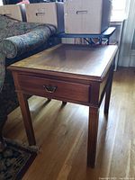 View of the Hickory Chair solid wood end table showing the side with the drawer, fluted legs, and wooden flooring beneath.