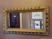 Full view of ornate rectangular gold gilt framed mirror hanging on a wall.