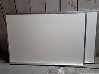 Two used white boards leaning against a wall, showing aluminum framed edges and clean writable surfaces.