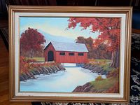 Frontal view of painting in mid-century wood frame showing a New England covered bridge over a river with autumn trees.