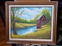 Frontal photo of the landscape painting showing the watermill by the creek, wood frame, and surrounding grasses and tree.